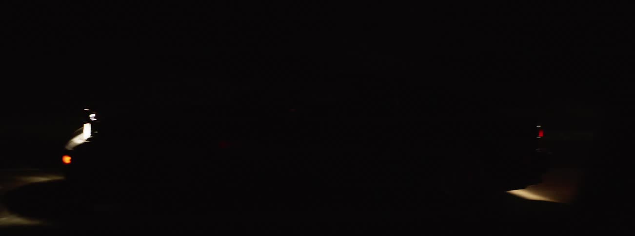 Headlight lights ground ahead of car moving along road in the night
