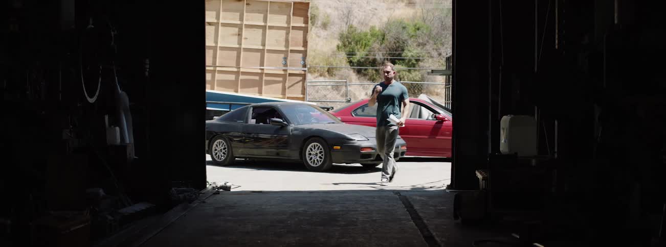 A man exiting a sports car and removing his sunglasses before walking into a garage and looking around