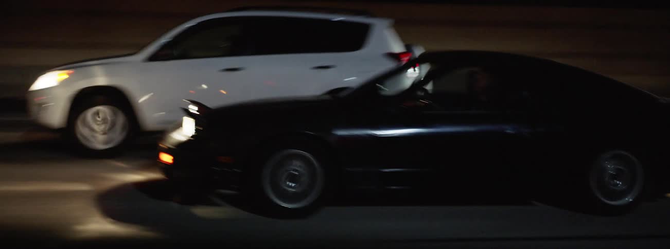 A black sports car speeds past other vehicles driving at night