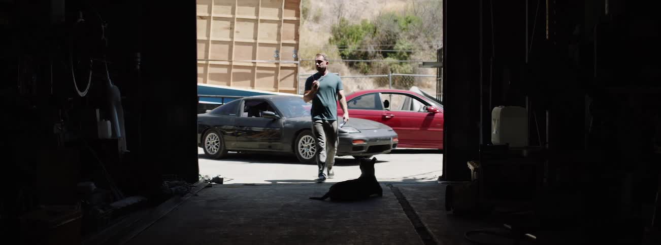 A white male walks into a garage and pets a dog