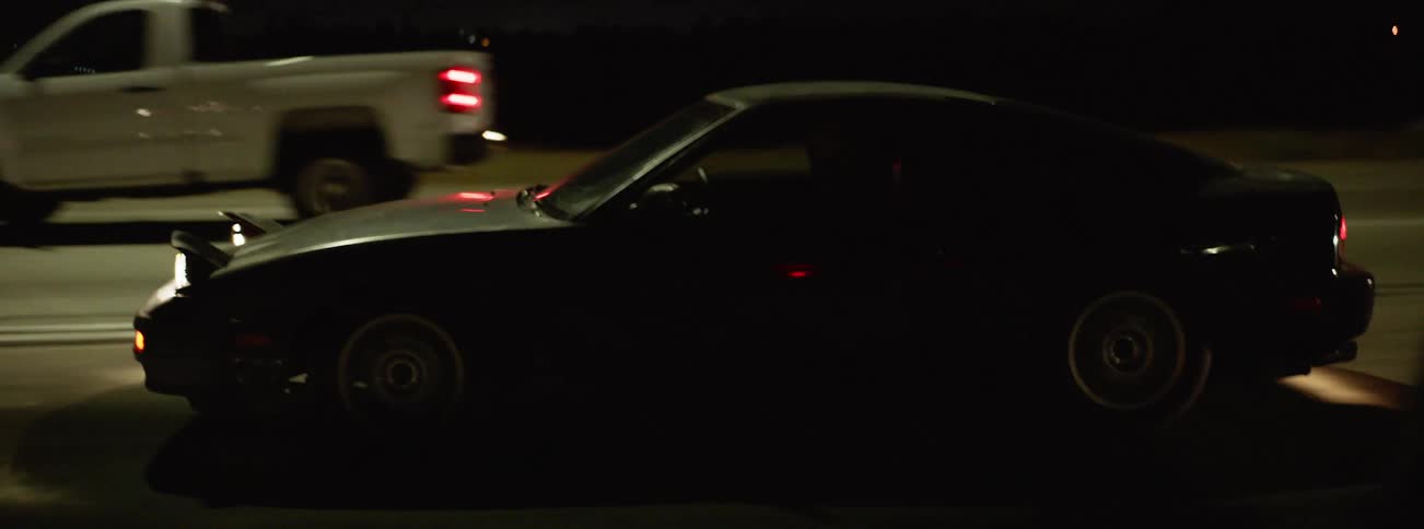 A driver in a sports car speeds down a road through traffic at night