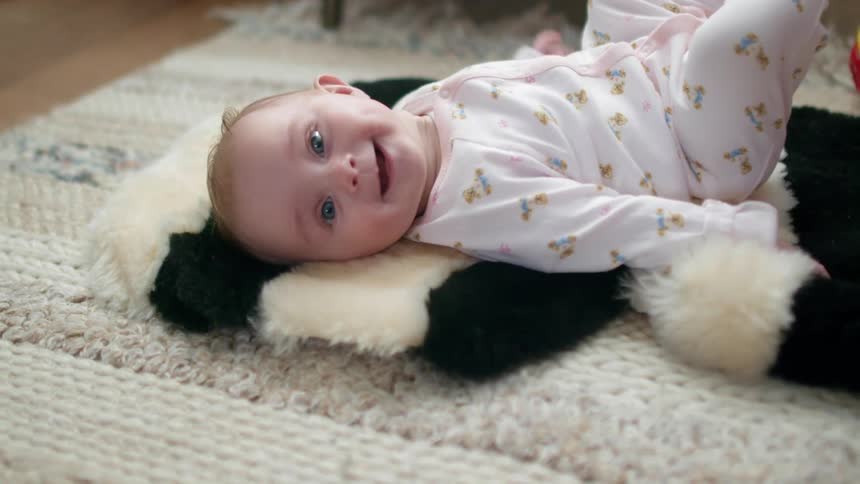 A baby lies on a rug and laughs and kicks her legs