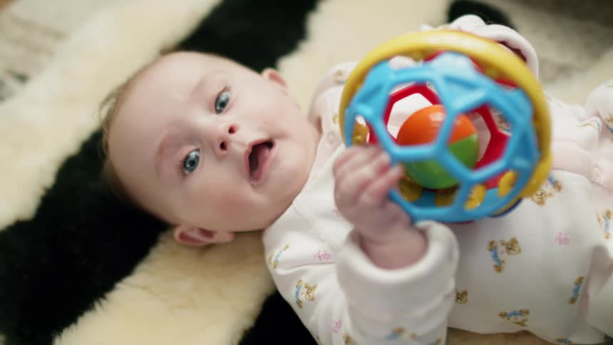 A baby holds a toy while lying on a rug