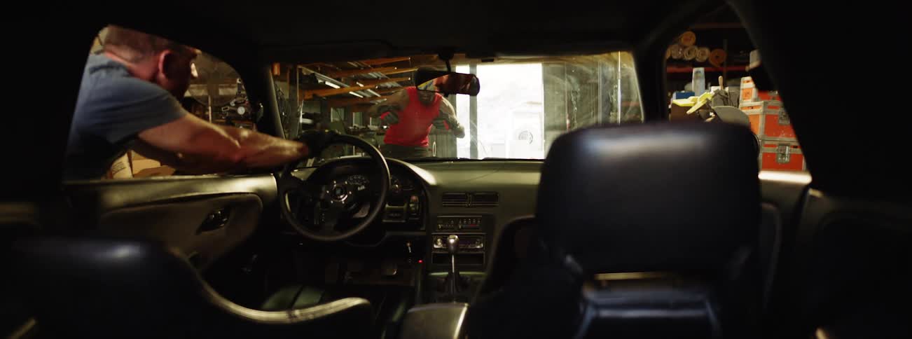 A man reaches in through the car window and pushes the car forward while another man guides him