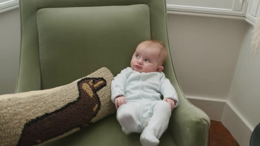 Baby sits in an armchair in the living room at home