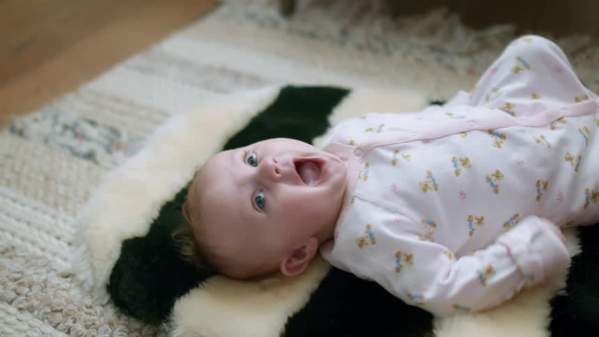A baby lies down on a furry striped rug as her father reaches out the touch her