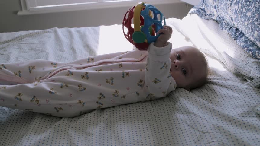 A baby lays in bed holding a toy ball