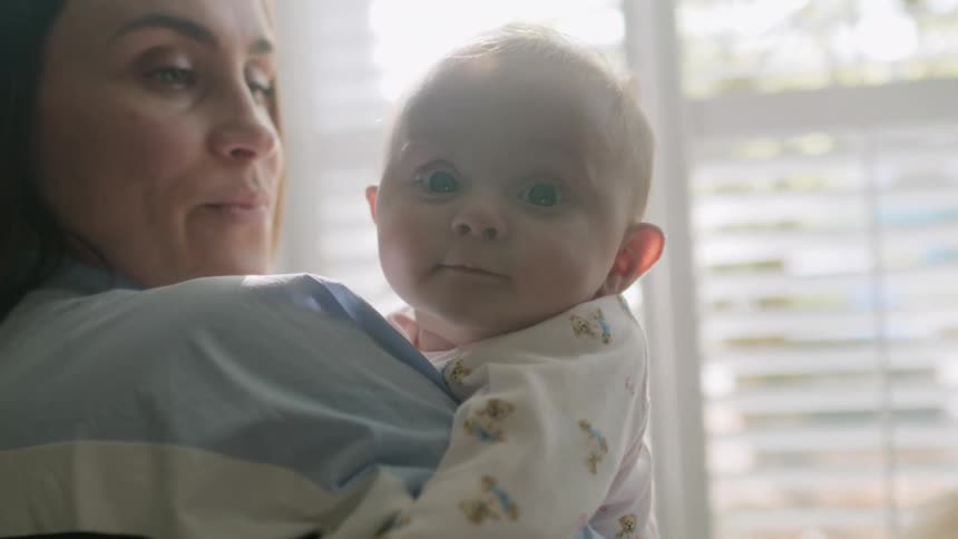 A mother smiles while holding her infant son at home