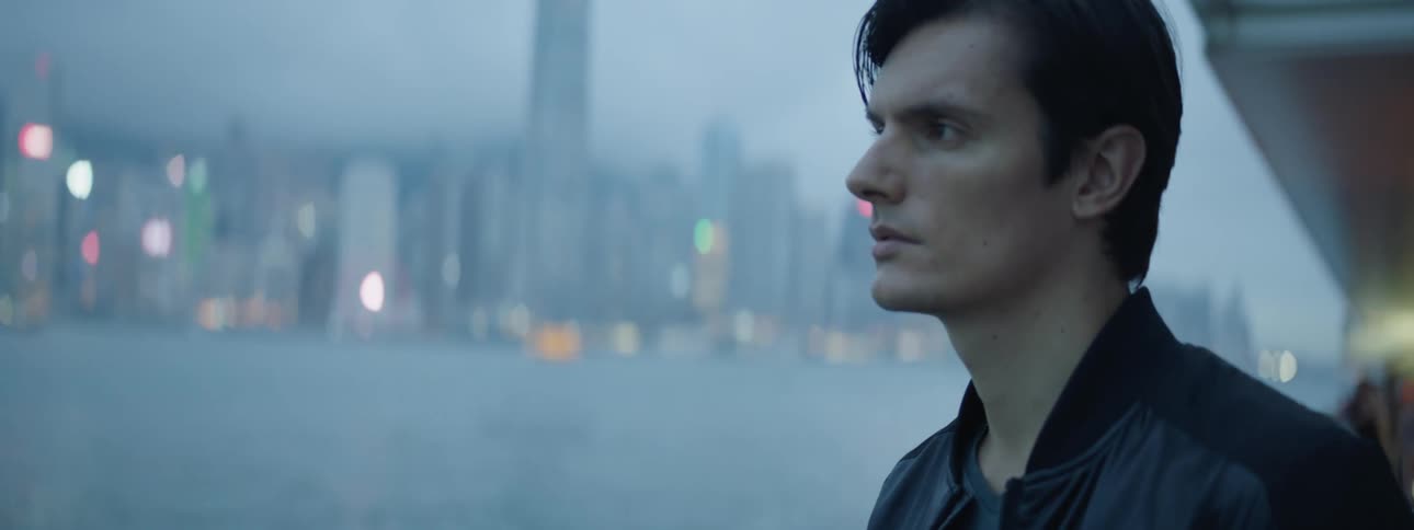 A white man stands outside a building and looks off into the distance