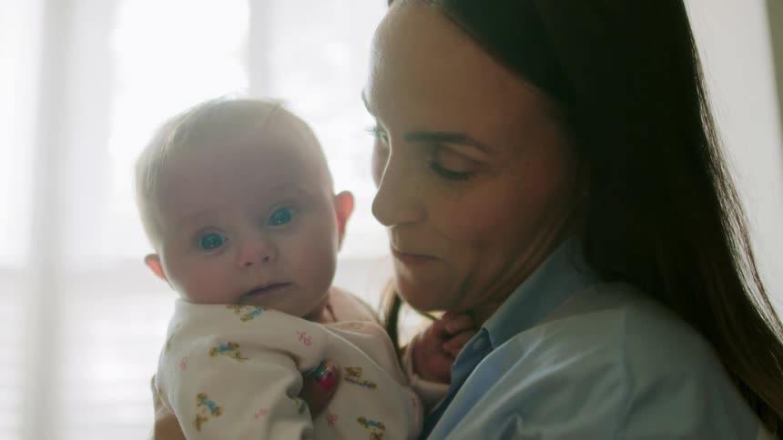 Mother cuddling infant blows raspberry on its cheek and smiles