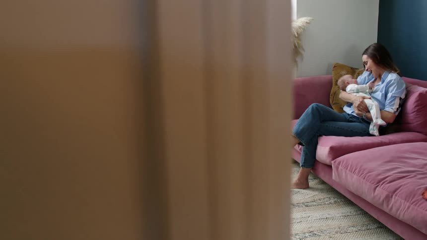 A mother holds and speaks to her baby while sitting on a couch in a living room