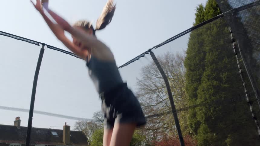 Female teenager jumping on a trampoline in the backyard performs a front handspring