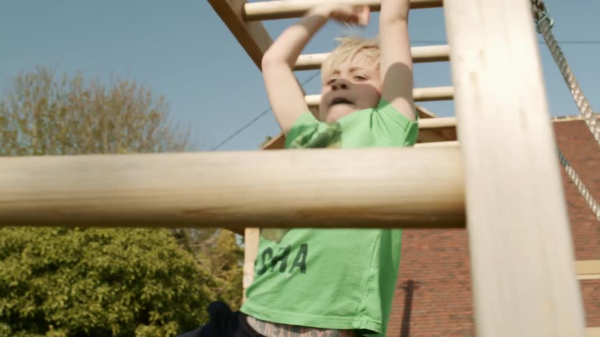 A boy playing on monkey bars with a building and trees in the background