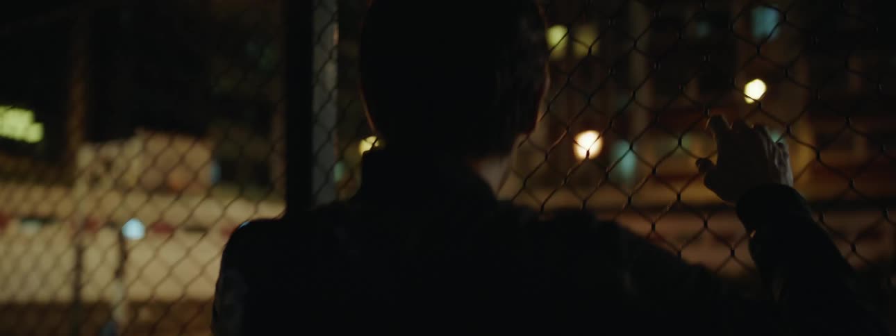 A man leans against the fence watching a basketball game