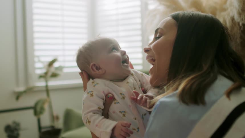 A mother plays with and kisses her newborn infant who laughs in response