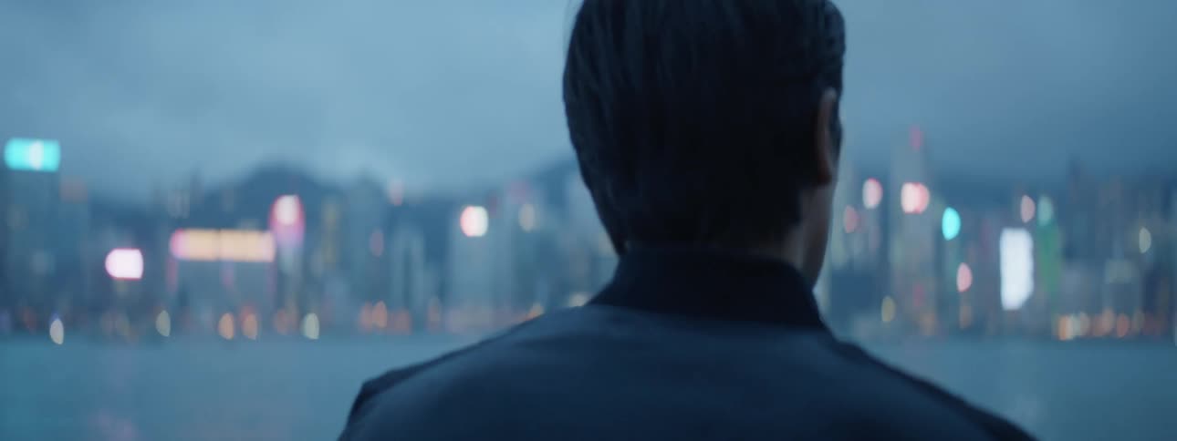 A man stands by the ocean near a city and looks around