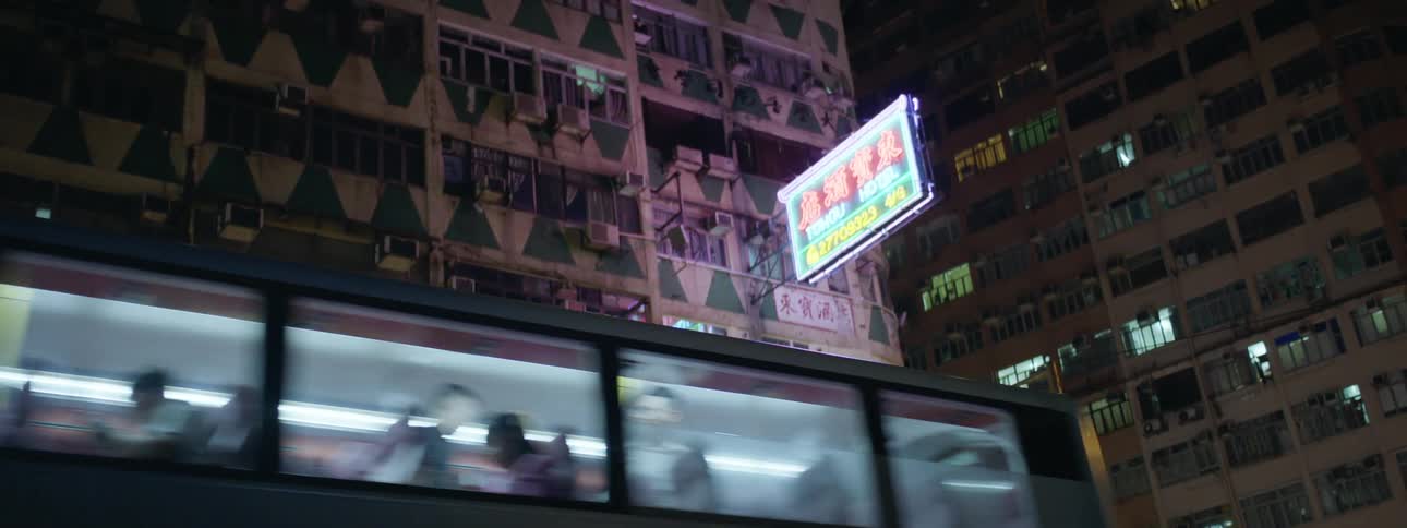 Public transportation drives by a downtown city building sporting a glowing neon sign