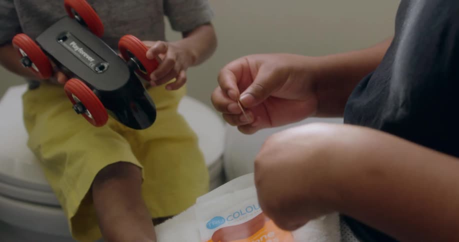A boy playing with a toy car while a man takes a bandaid from a package
