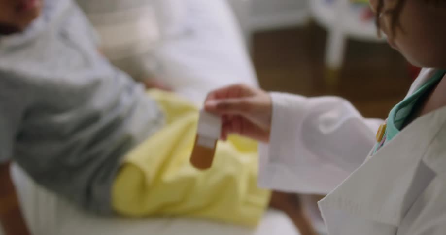 A young girl wearing a doctor coat opens a bandage for another child