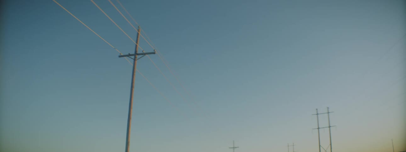 Car drives by power lines lining road under a clear blue sky