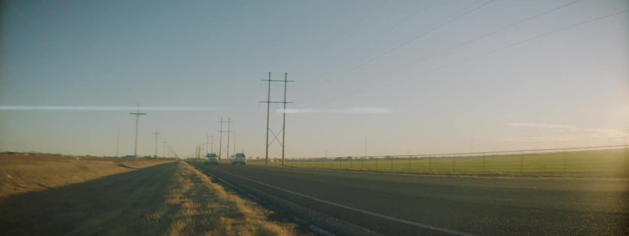 A road with vehicles next to a grassy field with the sky in the background