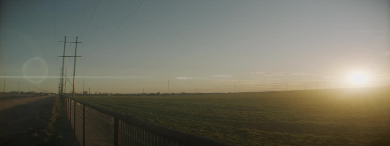 A car drives past a field with the sun setting