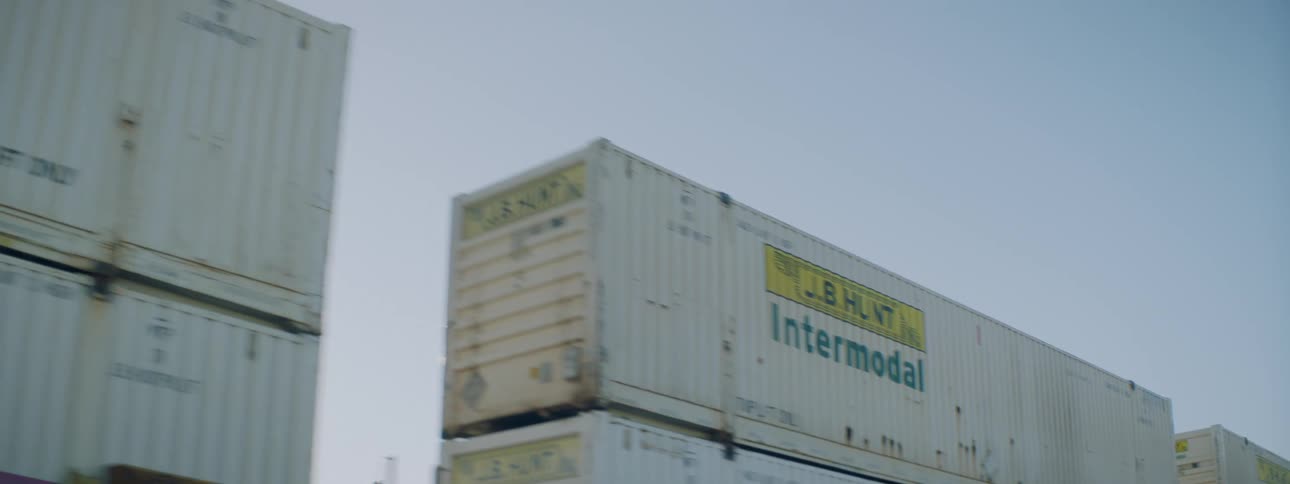Sun glares down on train carrying stacked cars under clear blue sky