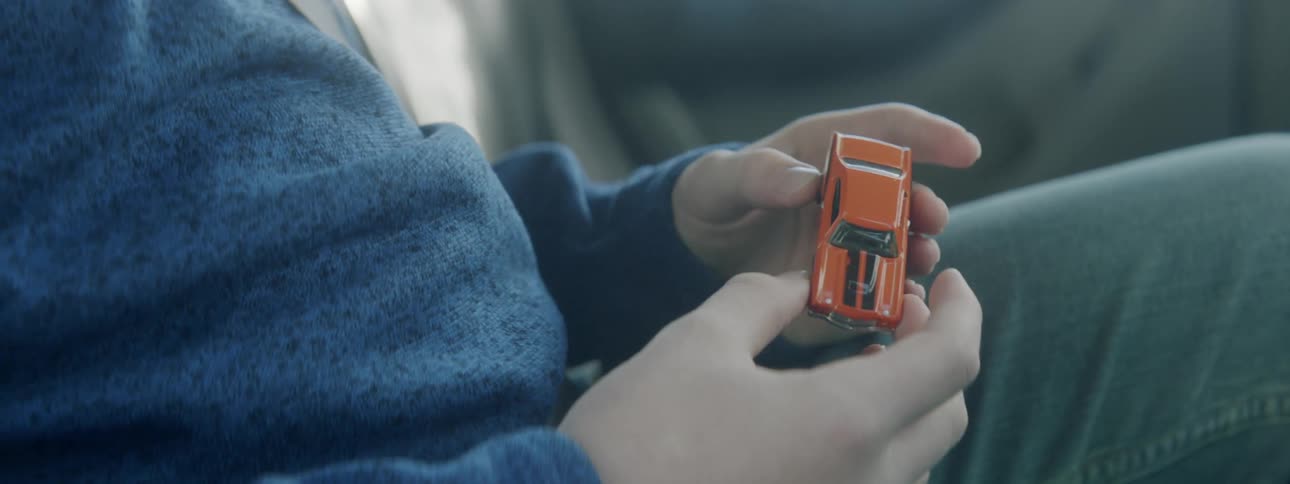 A boy sitting in the back of a moving vehicle while twirling a toy car in his hands