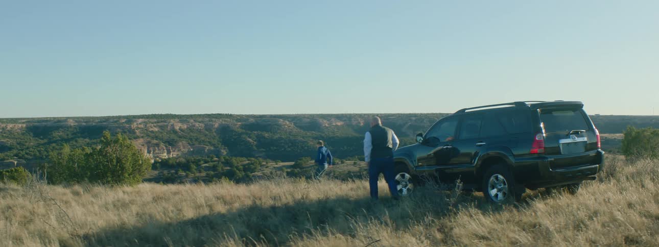 Two men get out of a car parked at the top of a hill and run down