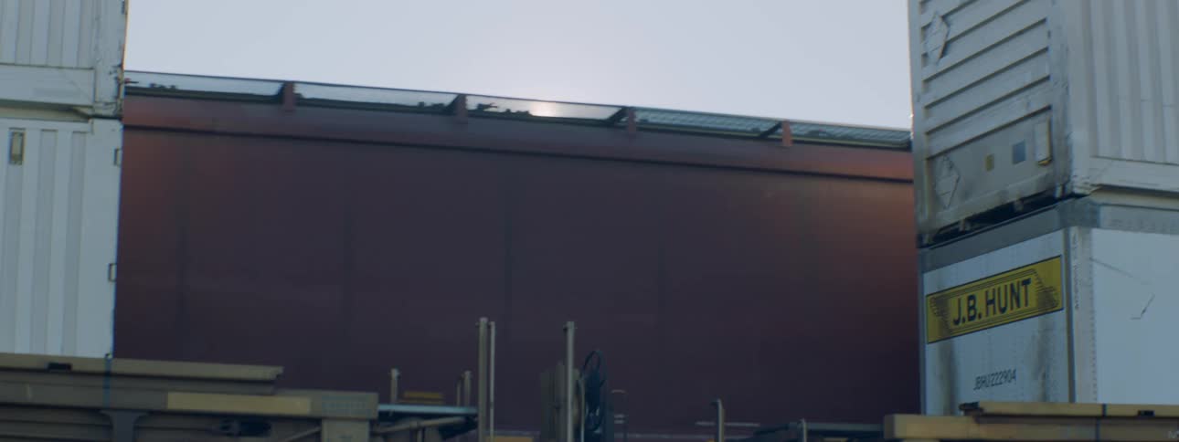 A train moves past stacked containers and wooden pallets