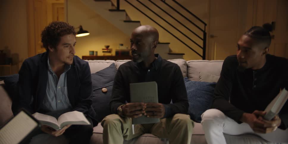 Three black men with books sit on a couch and smile and talk