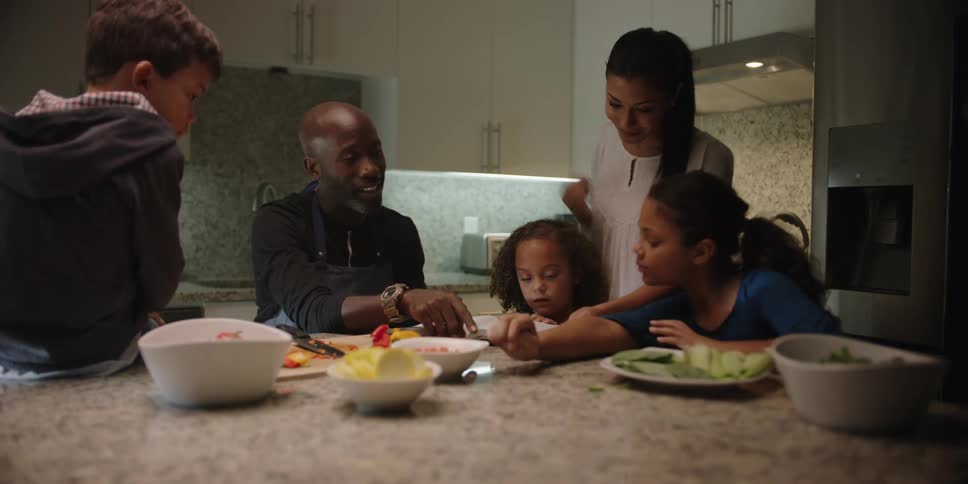 A black family sits around a counter top in a kitchen talking and eating a meal