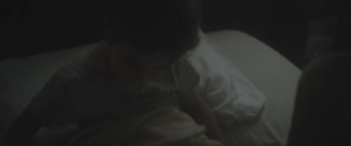 A child sits up in bed in a dark room