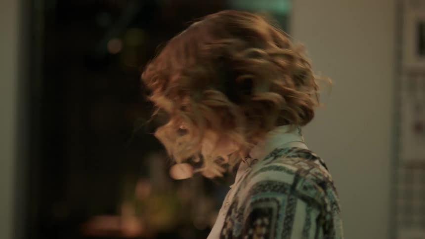 A woman stands up and looks around making her curly blonde hair bounce