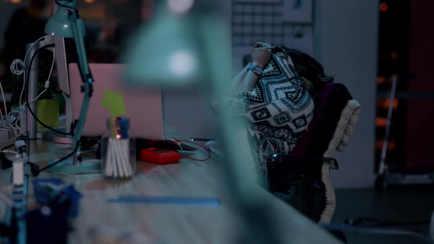 Woman sleeping on her desk in the office at night gets scared when a table lamp turns on