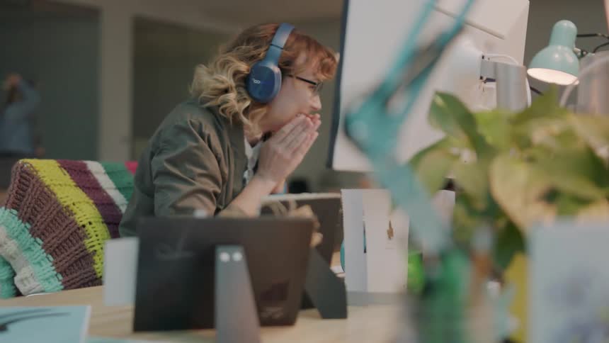 A woman in an office with headphones looking at a laptop