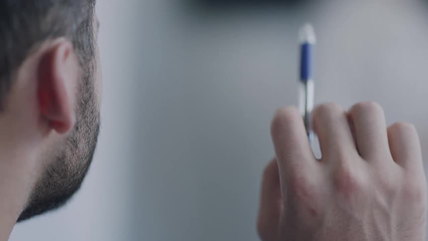A man twirls a pen around in his hand as he sits and listens