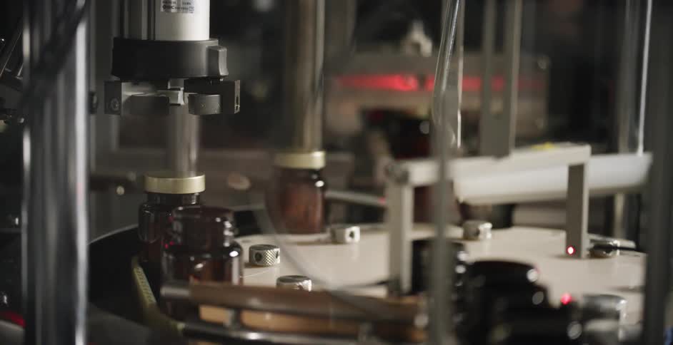 A machine screws lids on jars moving down an assembly line in a factory