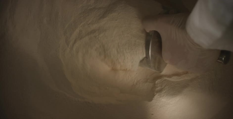 A person in lab gear scoops powder out of a container