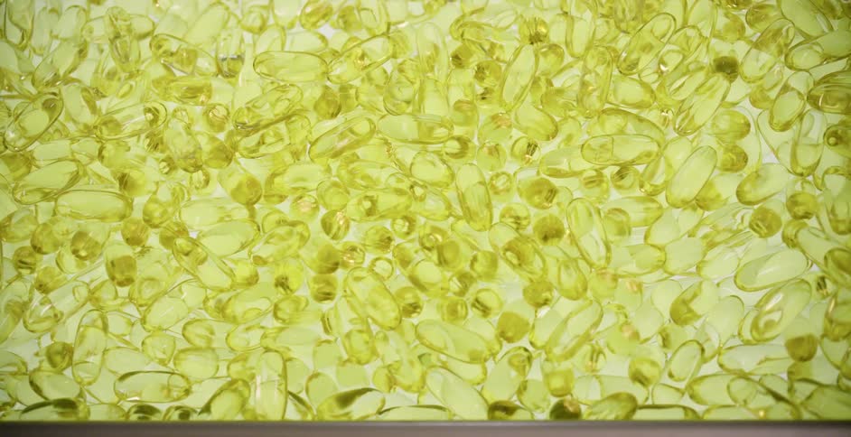 Yellow soft gel capsules on a back lit tray