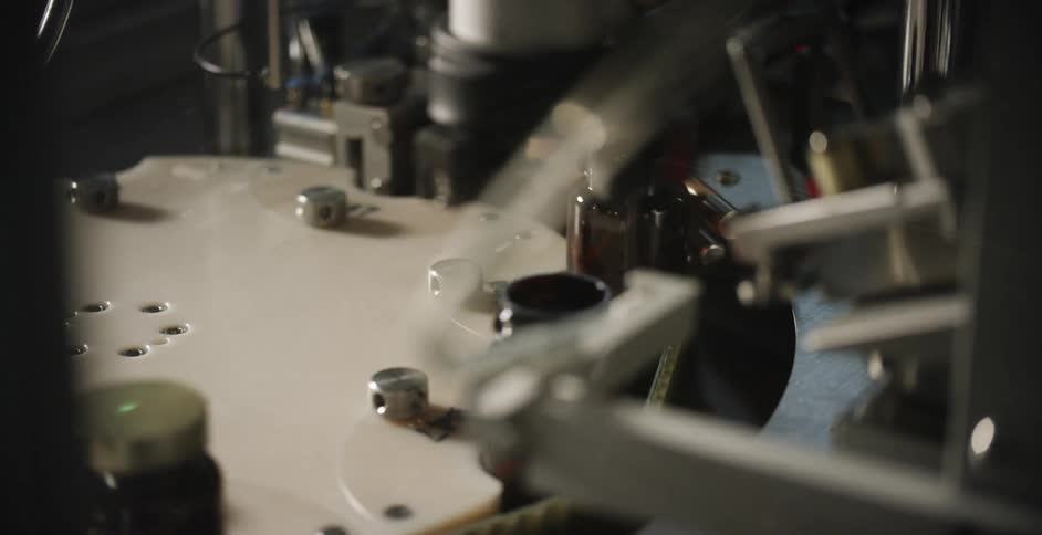 A machine screws lids on glass jars moving on an assembly line