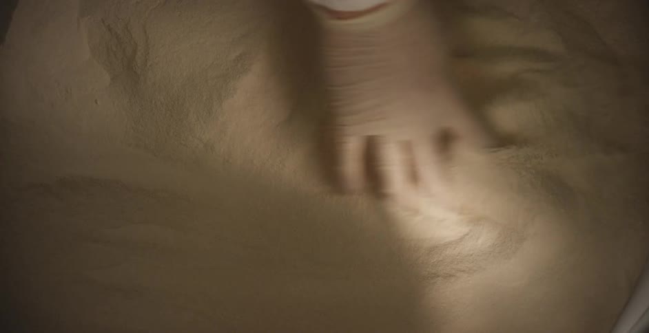 Hand wearing a medical glove moves the sand around with his fingers