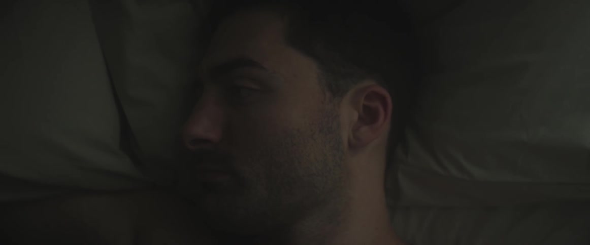 A man opens and closes his eyes on a bed