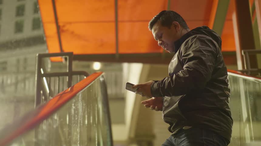 A man standing on an escalator talks and uses his cellphone