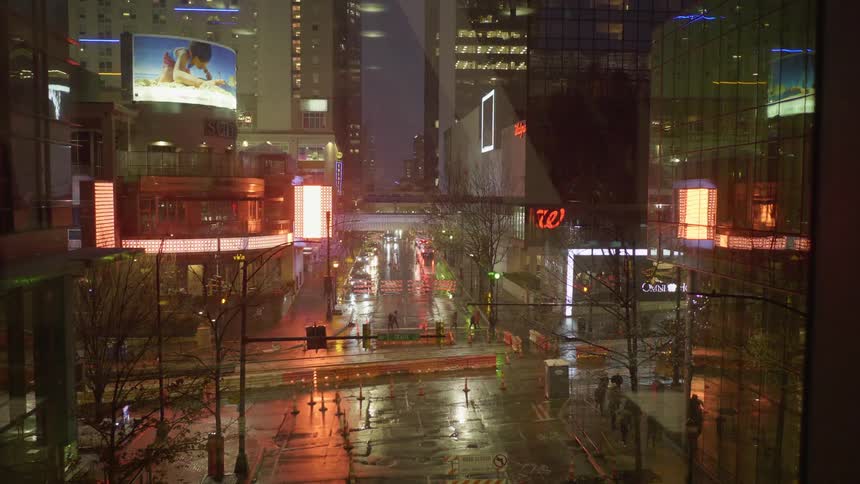Pedestrians walk along brightly lit downtown street bordered by skyscrapers