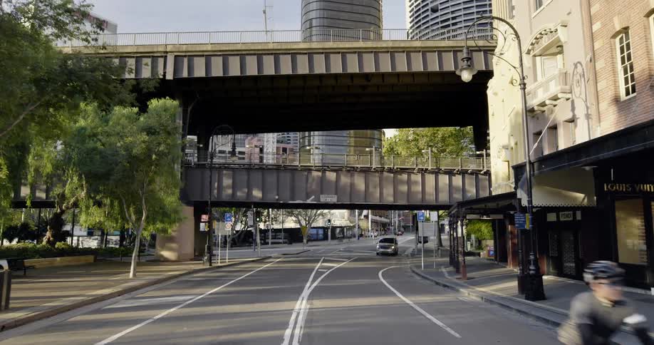 A person rides a bicycle on a city road underneath bridges