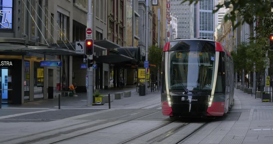 A red and black street car traveling through an intersection in a metropolis during the day