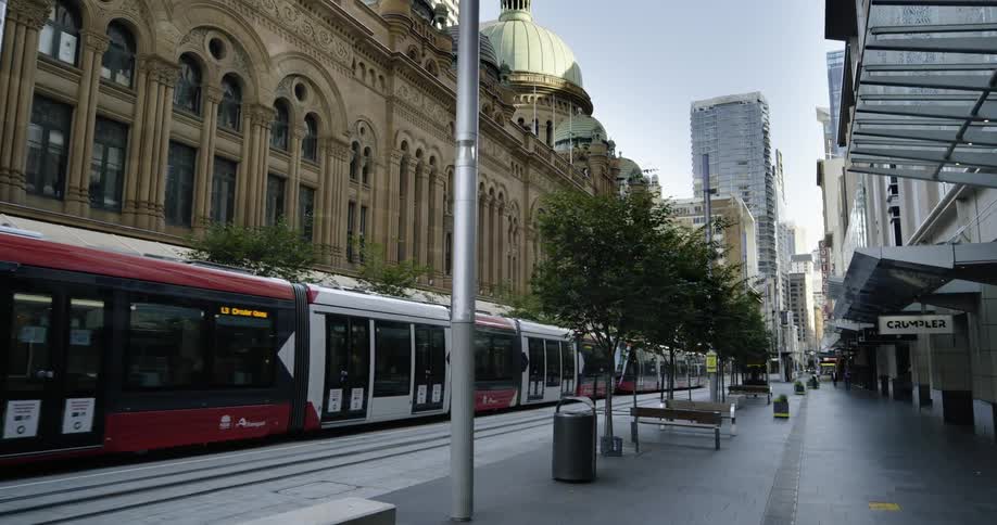 Long light rail train passes between storefronts with nearly empty sidewalks toward downtown