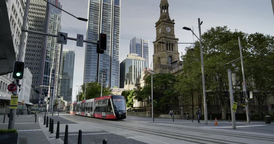 A modern train moves through the downtown of a city that has both old and new buildings and structures