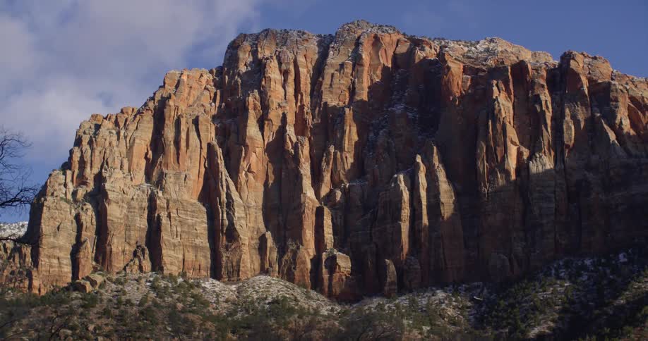 Bare trees stand in front of a large mountain with steep cliffs